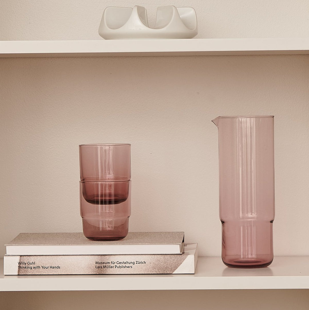 Set of minimalistic glass carafe and matching stackable drinking glasses in pink