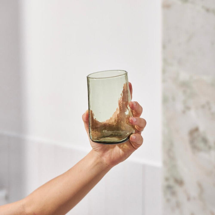 Hand holding a tall green drinking glass